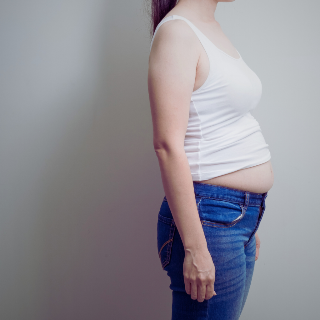 Woman with a bloated tummy wearing jeans and tank top.